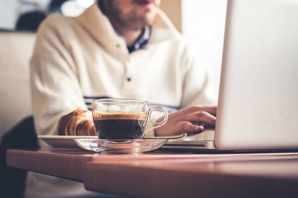 Persona adulta sentada en una mesa de trabajo con una taza, computadora y cuaderno, haciendo una pausa tranquila